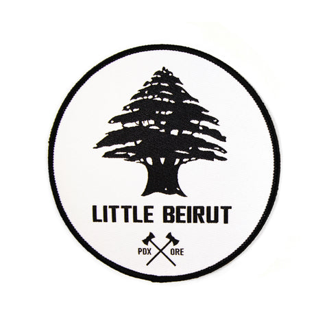 A white 5x5 patch with an embroidered design. The words "Little Beirut" above black crossed axes with PDX ORE on the sides, underneath a large black tree.