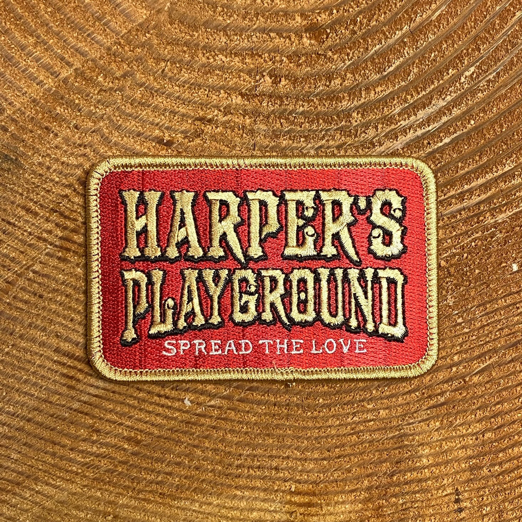 Maroon, rectangular patch with gold stitching reading "Harper's Playground" and in smaller letters underneath "Spread the Love"